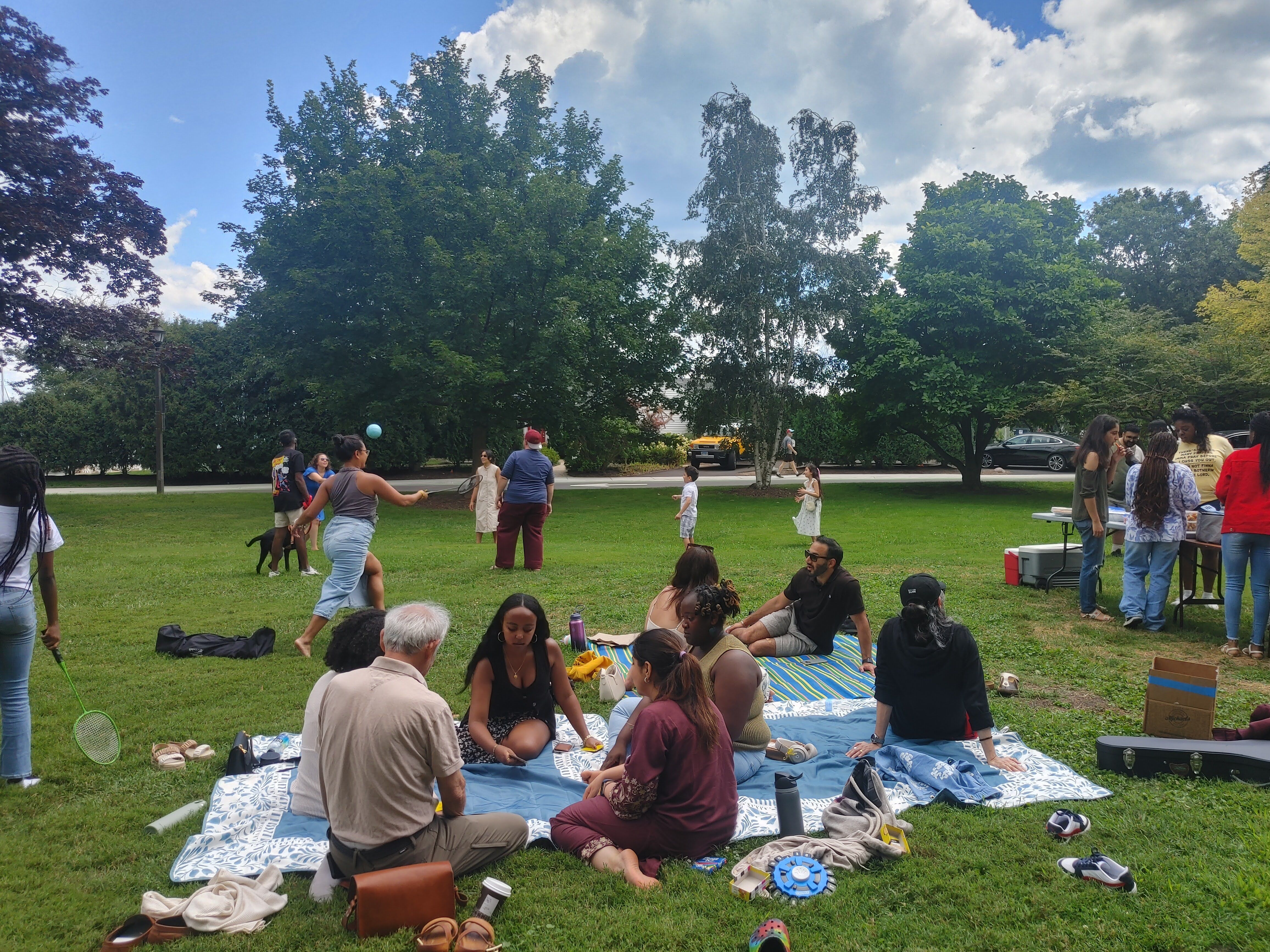 Adults and children gathering on blankets and playing in a park.